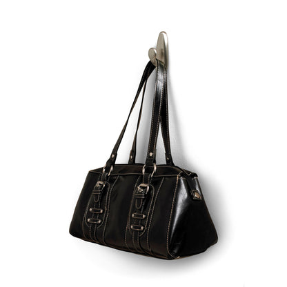 An einem Command™ Metallhaken "klassisch" der 3M Deutschland GmbH hängt eine schwarze Lederhandtasche mit Doppelgriffen und Zierschnallen. Die Tasche hat weiße Nähte und eine leicht glänzende Oberfläche.