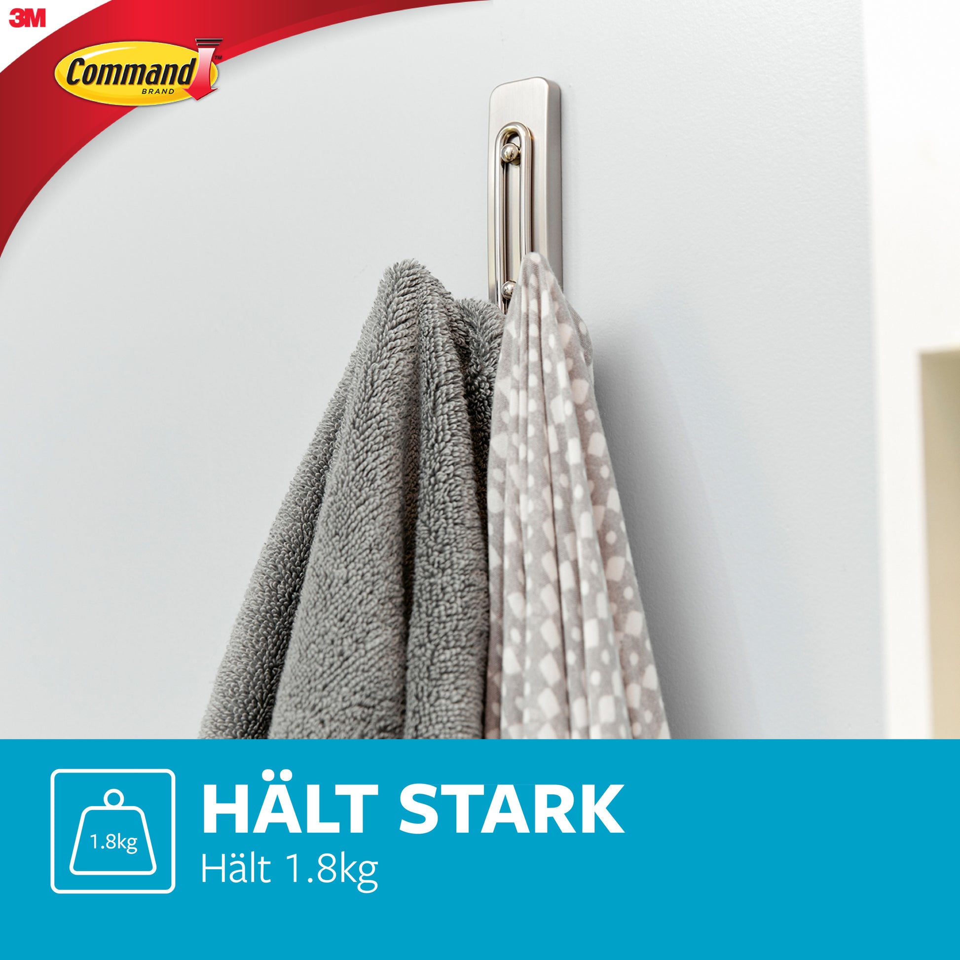 A Command™ Großer Badezimmer-Doppelhaken Nickel satiniert von 3M hält an einer weißen Wand zwei graue Handtücher (eins mit weißen Punkten). Im Bild steht: "HÄLT STARK Hält 1,8 kg" und das 3M Logo ist sichtbar.
