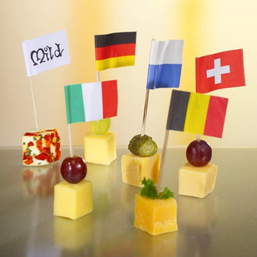 Six cheese cubes are decorated with PAPSTAR 200 decoration picks 8 cm from PAPSTAR GmbH and each is adorned with flags (Germany, Italy, France, Switzerland, Belgium, and “mild”) as well as garnishes like grapes and herbs – perfect finger food for the gastronomy.