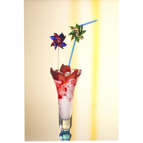 Ein hohes Glas mit einem rosa-weißen Frozen Drink, garniert mit Erdbeerstücken und zwei PAPSTAR 100 Deko-Pickern der PAPSTAR GmbH sowie einem blauen Strohhalm, auf hellem Untergrund mit gelbem Streifen.