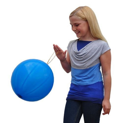 A smiling girl with long blonde hair and a blue-grey shirt plays with a large PAPSTAR punch balloon (Ø 40 cm, assorted colors, 3-set) from PAPSTAR GmbH against a white background.