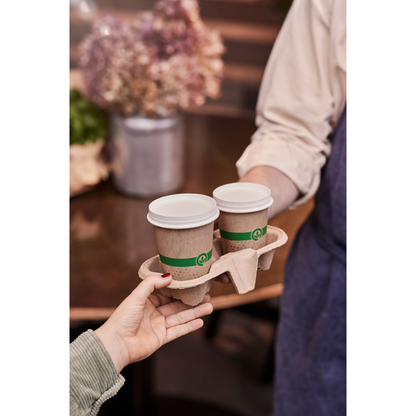 A person hands a person in an apron a cardboard drink carrier with two Duni Melli cups 240 ml multicolored from Duni GmbH (each with a white lid), in the background a blurred flower arrangement can be seen.