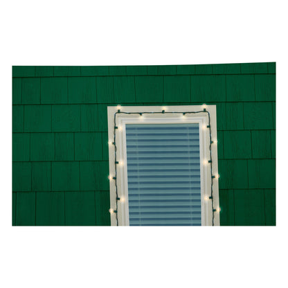 Ein Fenster mit geschlossenen Jalousien an einer grün geschindelten Wand ist mit weißen Lichtern umrandet, die mit 3M Command™ Outdoor Lichter-Clips (17017CLR-AWPU) von 3M Deutschland GmbH für eine zuverlässige Installation der Außenbeleuchtung sicher befestigt wurden.