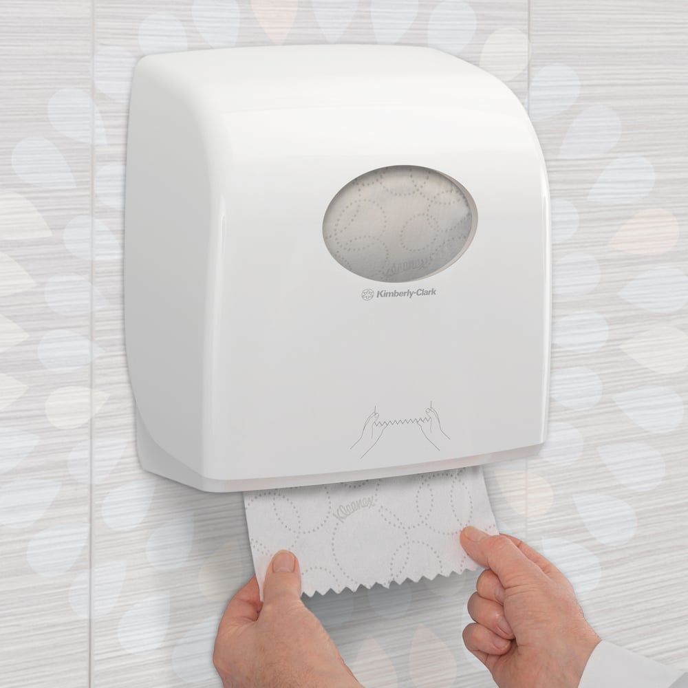 Someone pulls a Kleenex® Ultra™ Slimroll™ hand towel from a white, wall-mounted dispenser with a viewing window and symbols in a tiled restroom. Product: 6-roll carton from Kimberly-Clark GmbH.
