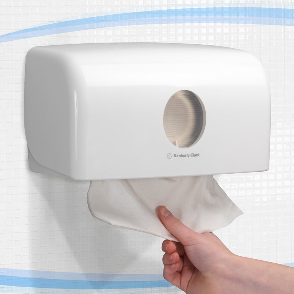 A hand entnimmt ein Handtuch aus dem weißen Aquarius™ Spender für gefaltete Handtücher (MultiFold, klein) von Kimberly-Clark GmbH, der wandmontiert an einer gefliesten Wand hygienische Ausgabe ermöglicht.