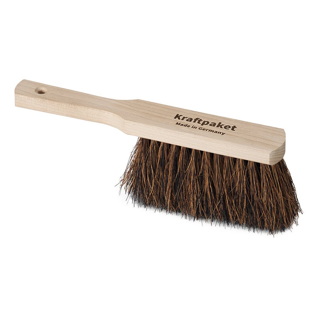 Der Nölle Profi Brush Handfeger 30 cm von Nölle Profi Brush Bürsten- & Pinseltechnik e.K. hat einen hellen Holzstiel mit "Kraftpaket Made in Germany", dichte dunkle Borsten aus Arenga- und Kokosfasern und ein Loch zum Aufhängen.