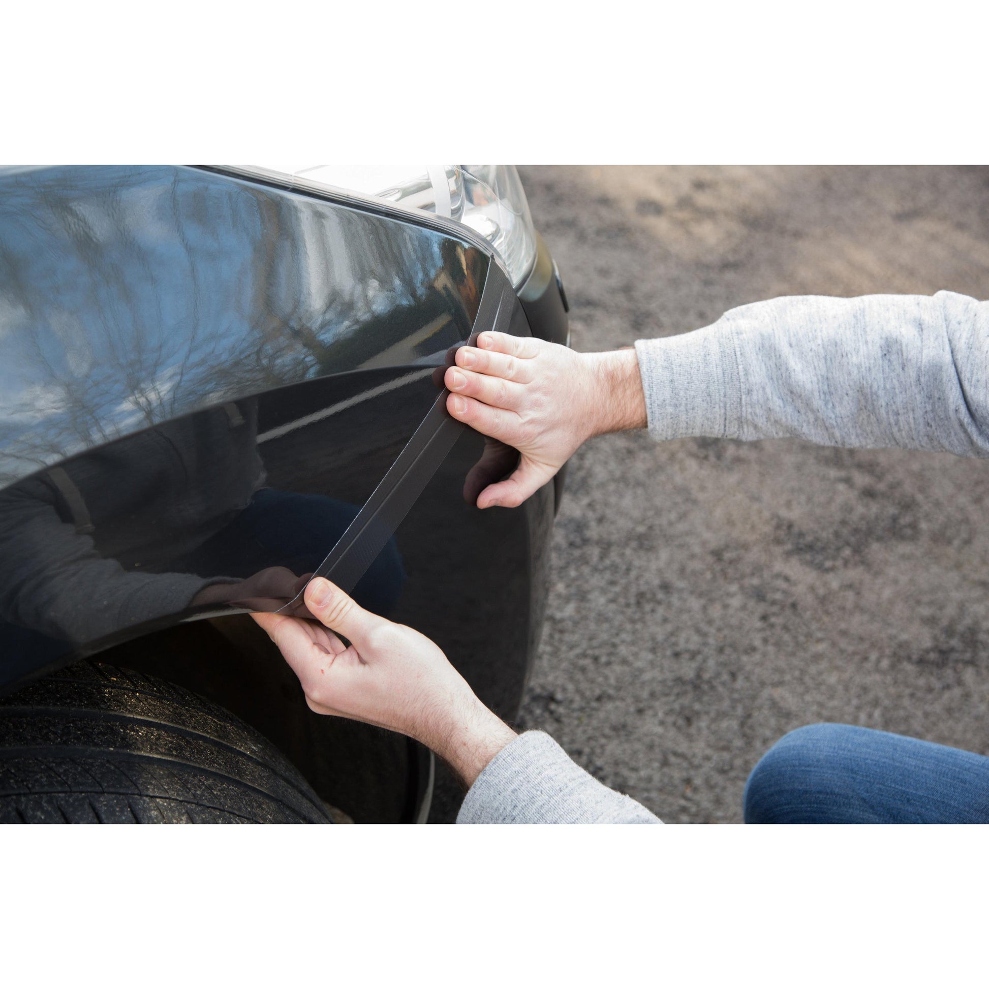 Eine Person bringt das Scotch® Extremium™ No Residue Hochleistungs-Gewebeklebeband (18,2 m x 48 mm) von 3M an der vorderen Kotflügelkante des Autos an und drückt es auf den Lack, um die Oberfläche zu schützen, ohne Rückstände zu hinterlassen.