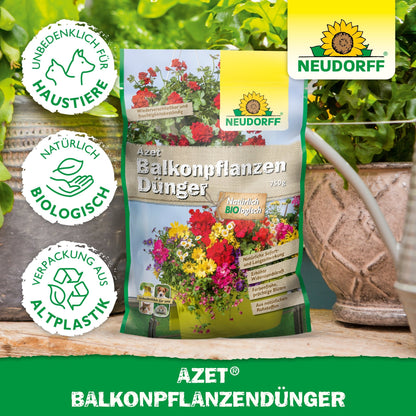 Una bolsa de fertilizante para plantas de balcón Azet de Neudorff Shop está sobre una mesa entre plantas en macetas y jardineras de balcón. El empaque muestra flores, texto y símbolos de protección animal, ingredientes biológicos y envases de bioplástico.