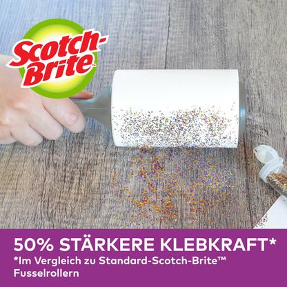 Eine Hand nutzt den Scotch-Brite™ Pet Extra Sticky* Roller für Tierhaare von 3M Deutschland GmbH (48 Blatt), um verschüttete Glitzer auf einer Holzoberfläche zu entfernen. Deutsche Werbung: 50 % stärkere Klebkraft als Standardmodelle.