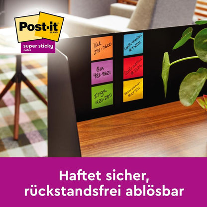 Close-up of a monitor with Post-it® Super Sticky Notes Cube, Yellow, 76 mm x 76 mm from 3M Deutschland GmbH, covered with handwritten names and phone numbers. In the background, a plant, a table, and a patterned carpet are visible. The German text appears below.