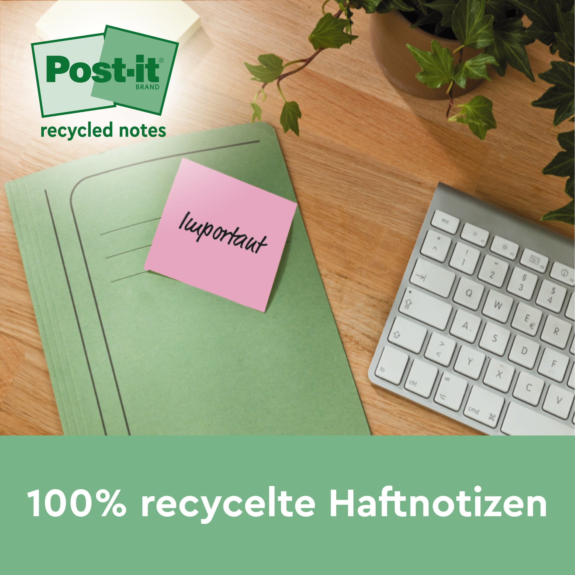 Ein grüner Ordner mit einem rosa Post-it® Recycling-Zettel der 3M Deutschland GmbH (38 mm x 51 mm, 100 Blatt/Block, 100% PEFC) liegt auf einem Holztisch neben einer weißen Tastatur und einer Topfpflanze.