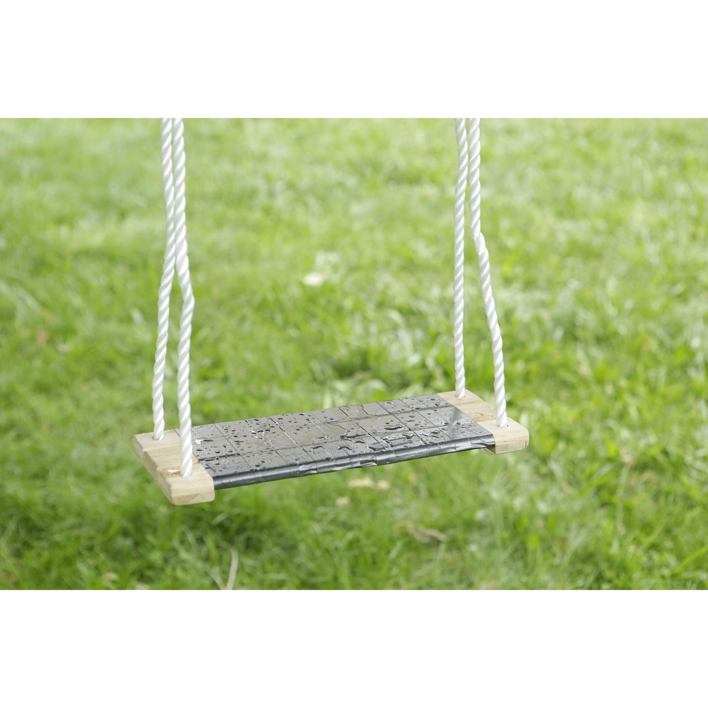 Nahaufnahme einer einfachen Schaukel mit Holzsitz und weißen Seilen, gesichert mit Scotch® Extremium™ All Weather Hochleistungs-Klebeband (27 m x 48 mm) von 3M Deutschland GmbH, die über grünem Gras mit Wassertropfen hängt.