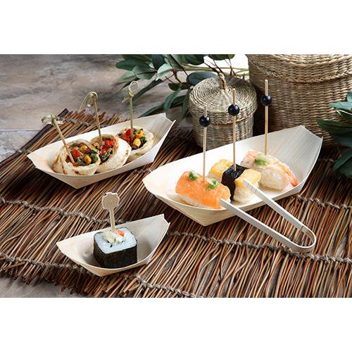 Drei PAPSTAR 50 Fingerfood - Schalen, Holz "pure" "Schiffchen" der PAPSTAR GmbH, gefüllt mit verschiedenen Sushi- und Snackspießen, sind auf einer geflochtenen Matte mit belaubten Zweigen und Weidenkörben im Hintergrund arrangiert.