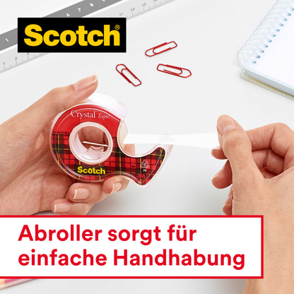 Eine Person spendet Scotch® Crystal Klebeband (19 mm x 25 m, 1 Rolle + 8 m GRATIS) von 3M Deutschland GmbH. Im Hintergrund sind rote Büroklammern, ein Lineal und ein Spiralnotizbuch zu sehen. Deutscher Text: "Abroller sorgt für einfache Handhabung.
