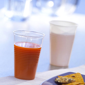 A Starpak 25 drinking cup, PP 0.2 l (Ø 7.03 cm · 9.9 cm), filled with orange juice, stands in the foreground next to a white cup with a light drink; at the bottom right, a blue plate with food can be seen - ideal for on the go.