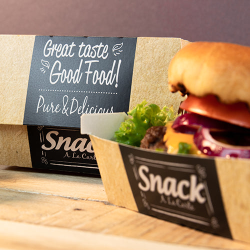 Ein Papptablett mit der Aufschrift "Snack A La Carte" enthält einen Hamburger mit Salat, Tomate und Zwiebel. Im Hintergrund steht eine PAPSTAR 50 Burgerboxen, Pappe "pure" "Good Food" von PAPSTAR GmbH: Guter Geschmack Good Food! Pur & Lecker.