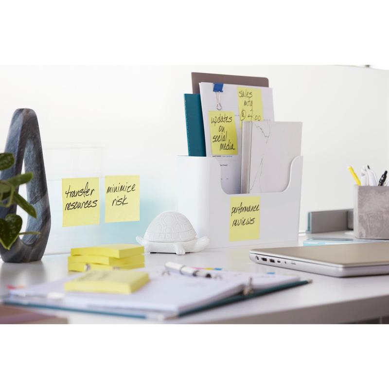 A modern office desk with a laptop, stationery, a white document tray, a small white turtle figurine, and 3M Deutschland GmbH Post-it® Super Sticky Notes Cube (Yellow, 76x76 mm) with the inscriptions "Transfer resources", "Minimize risk", and "Performance assessment".