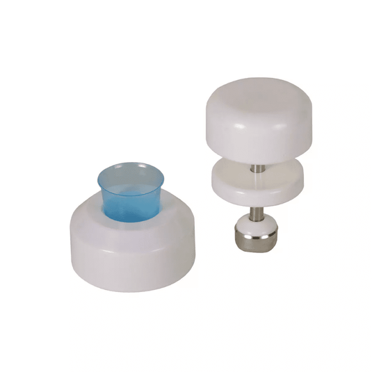 Two white plastic kitchen utensils are shown against a white background. The utensil on the left is cylindrical in shape and has a blue plastic insert, while the utensil on the right is an AMPri tablet crusher for medicine cups manufactured by AMPri Handelsgesellschaft mbH, consisting of two white discs connected by a stainless steel rod with a metal base.