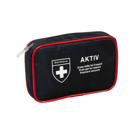 Un kit de primeros auxilios compacto de color negro con ribetes rojos y cremallera, un logotipo con una cruz blanca y las inscripciones «Holthaus Medical AKTIV» y «Erste-Hilfe für Freizeit / First-aid for Leisure / Premiers secours» en la parte delantera. Perfecto tanto para llevar de viaje como para tener en casa.