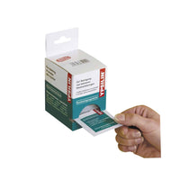 Una mano saca una toallita desinfectante para heridas Holthaus Medical YPSILIN® de un dispensador de cartón. El envase lleva un texto en alemán y la caja es de color blanco y verde, con información sobre el producto claramente visible y el nombre de la marca Holthaus Medical GmbH & Co. KG.
