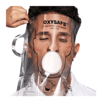 One person is wearing a transparent Holthaus Oxysafe® emergency ventilation mask manufactured by Holthaus Medical GmbH & Co. KG and has their eyes closed while another person adjusts the mask. The product includes instructions and diagrams printed on the plastic surface.