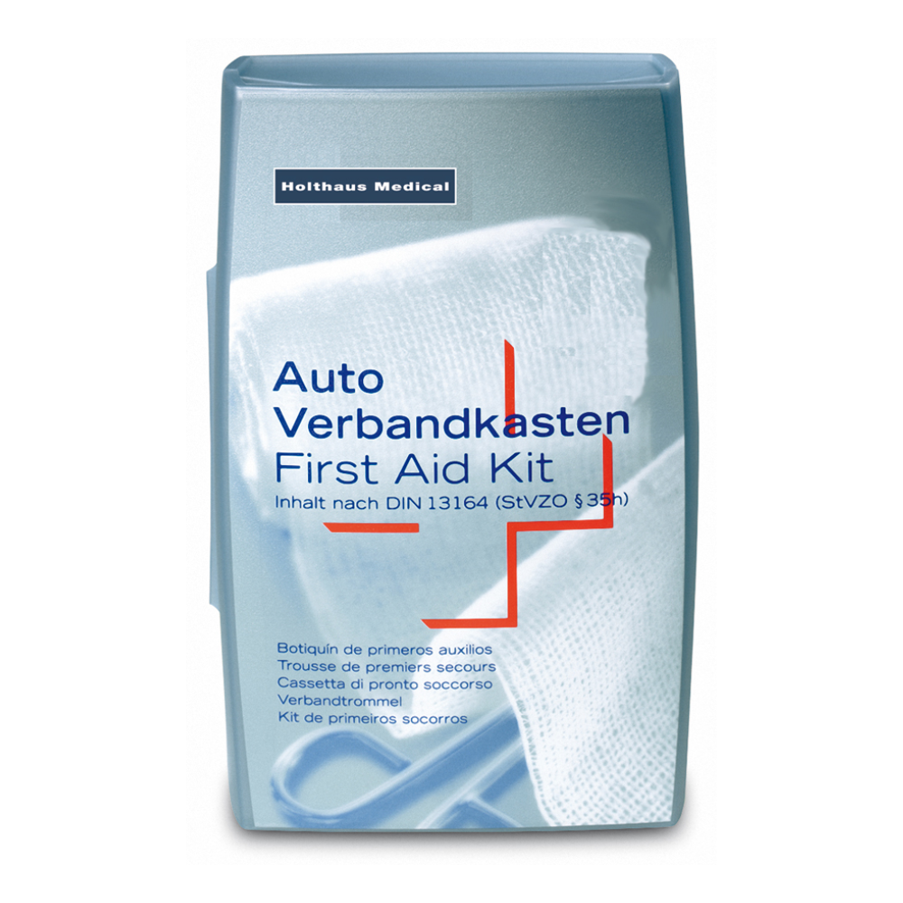 A silver Holthaus Silver First Aid Kit from Holthaus Medical GmbH & Co. KG. The text on the cover is multilingual with the indication "Car First Aid Kit / First Aid Kit" and points out that it complies with DIN 13164 (StVZO §35h). In the background, a white medical bandage can be seen, ideal for medical emergencies.
