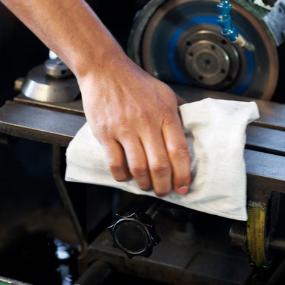 A person wipes a metal surface of a machine with a roll of Tork 570137 Extra Strong Industrial Cleaning Cloths W1 W2 W3 1-ply. Parts of the machine such as wheels and knobs are visible, emphasizing the effectiveness of these reusable cloths from TORK – Essity Professional Hygiene Germany GmbH in maintaining cleanliness and efficiency.