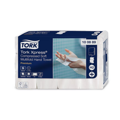 Un paquete de toallas de mano multifold comprimidas suaves Tork Xpress® Premium H2 de 2 capas, fabricadas por TORK – Essity Professional Hygiene Germany GmbH, está destinado a la dispensación hoja a hoja. El empaque azul y blanco muestra la imagen de una mano usando una toalla suave, lo que subraya la calidad premium de estas toallas de papel.