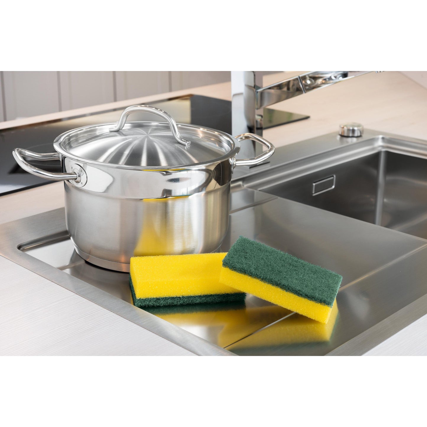 Ein Edelstahltopf mit Deckel steht neben der Spüle. Daneben stehen drei Schwämme, darunter ein 3M Deutschland GmbH Scotch-Brite® Classic Reinigungsschwamm XXL (6 Stück pro Packung). Im Hintergrund ist ein moderner Wasserhahn zu sehen.