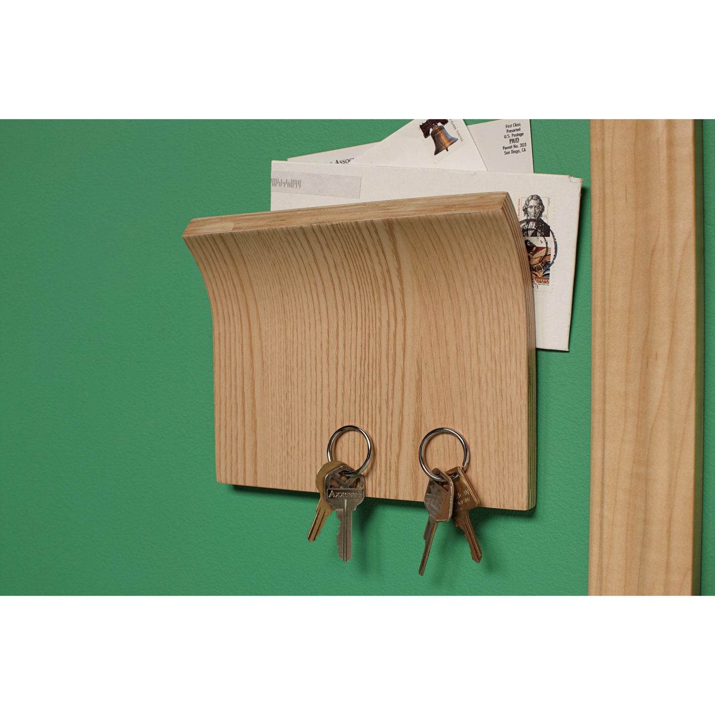 Ein hölzerner Wandbriefkasten mit Haken für Schlüssel wird mit dem Scotch-FIX™ Doppelseitigen Innenmontageband der 3M Deutschland GmbH an einer grünen Wand befestigt.