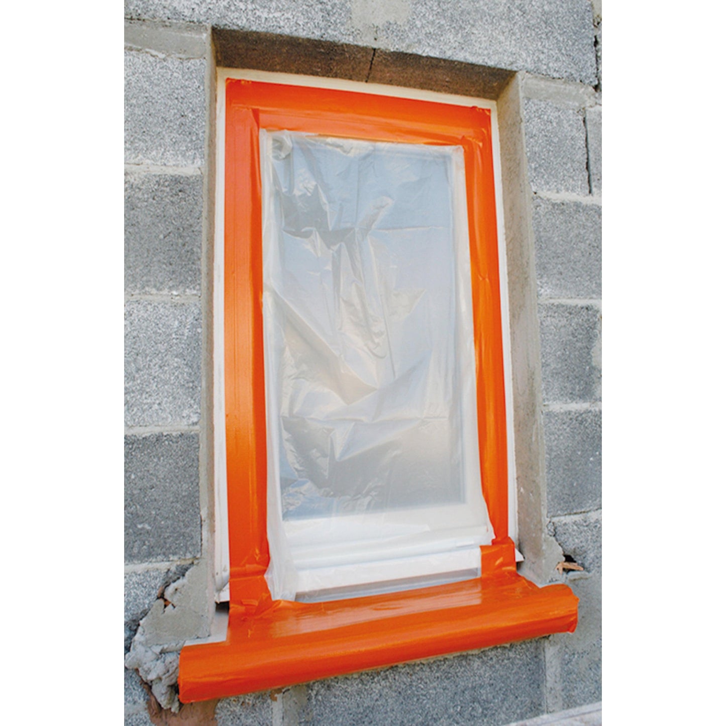 Ein Fenster an einer grauen Backsteinmauer ist mit einer durchsichtigen Kunststofffolie abgedeckt und mit dem Scotch® High Visibility Klebeband, orange, 25 m x 48 mm von 3M Deutschland GmbH eingefasst, wahrscheinlich zum Schutz bei Bau- oder Malerarbeiten.
