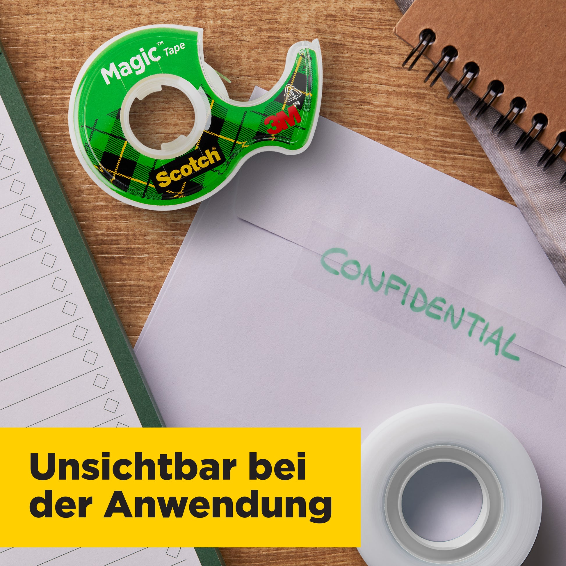 Ein grünes Scotch® Magic™ Unsichtbares Klebeband Nachfüllpackung (1 Rolle, 19 mm x 25 m, 3M Deutschland GmbH) in einem Spender liegt mit einem "CONFIDENTIAL"-Umschlag, einem Notizblock und einem Spiralnotizbuch auf einem Schreibtisch. Gelbes Transparent: "Unsichtbar bei der Anwendung.