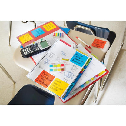 En un pupitre de aula hay cuadernos, un planificador con 3M Post-it® Index Strong Ablagetabs (Mini, amarillo, rojo, azul y verde), calculadora, bolígrafos, resaltadores y carpetas; sillas vacías lo rodean y las pestañas ayudan a organizar documentos.