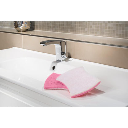 A white sink with a chrome faucet shows the Scotch-Brite® Bath XXL cleaning sponge from 3M Deutschland GmbH, pink on one side and white on the other, ideal for removing limescale deposits. Beige and light brown tiles appear in the background.