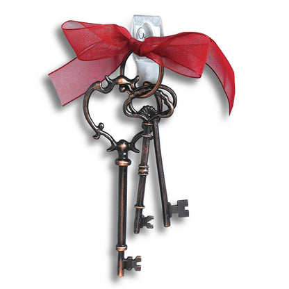 Drei verschnörkelte, antik anmutende Schlüssel an einem Schlüsselbund mit rotem Band hängen an einer weißen Wand mit 3M Deutschland GmbH Command™ Mini-Haken, transparent, mit transparenten Strips, 17006CLRFGN-perfekt für Aufbewahrung ohne Bohren.