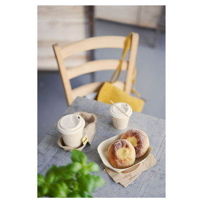 Sobre una mesa hay dos piezas de repostería espolvoreadas con azúcar en una bandeja y dos vasos de café Duni 'Sweet Bedruckte Bagasse' con tapa de Duni GmbH. Un bolso amarillo cuelga de una silla de madera, mientras que una planta verde parcialmente visible en primer plano resalta el sutil tema de la sostenibilidad.